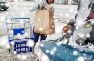 A woman loads grocery bags from her cart into her trunk, in the snow